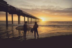 秋の夕暮れのビーチでサーフボードを抱えて歩く初心者サーファー