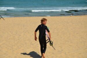 ウェットスーツを着てビーチを歩く男の子