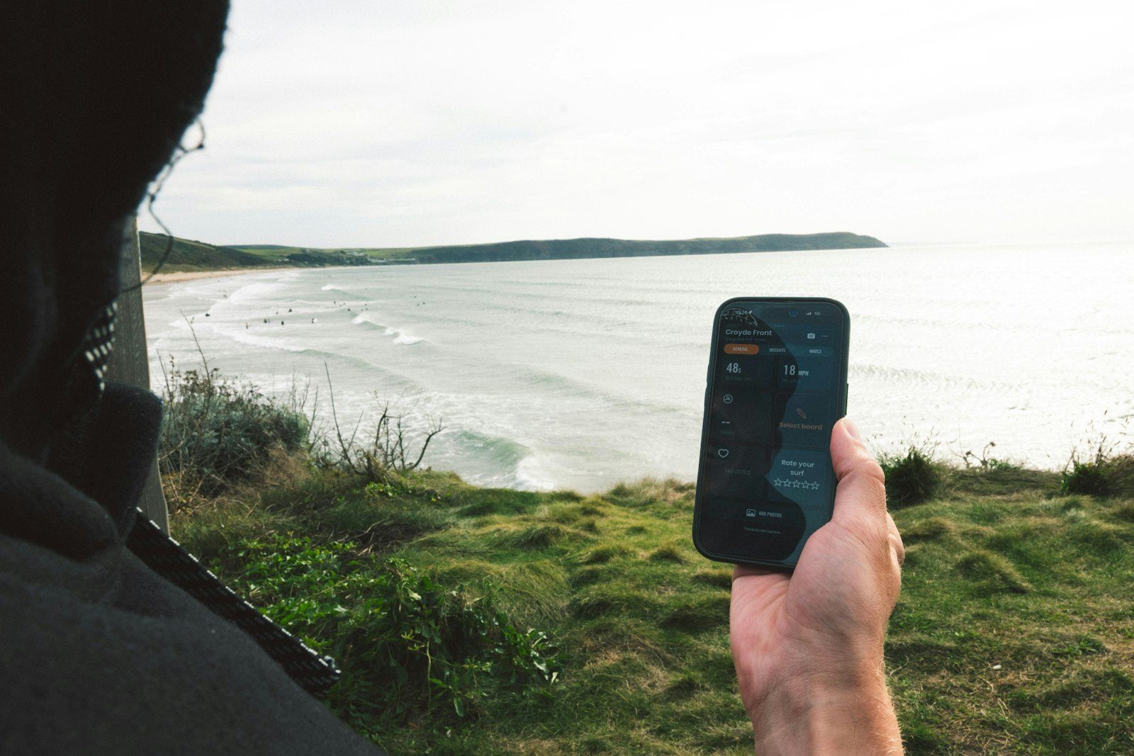 スマホで波情報を確認しながら海を見下ろすサーファー