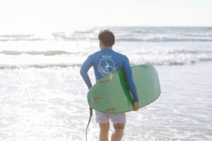 ラッシュガードを着てサーフボードを持ち海へ向かうメンズサーファー