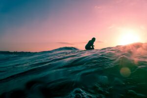 夕日の海でサーフィンするサーファー｜飲む日焼け止めで内側からUVケア
