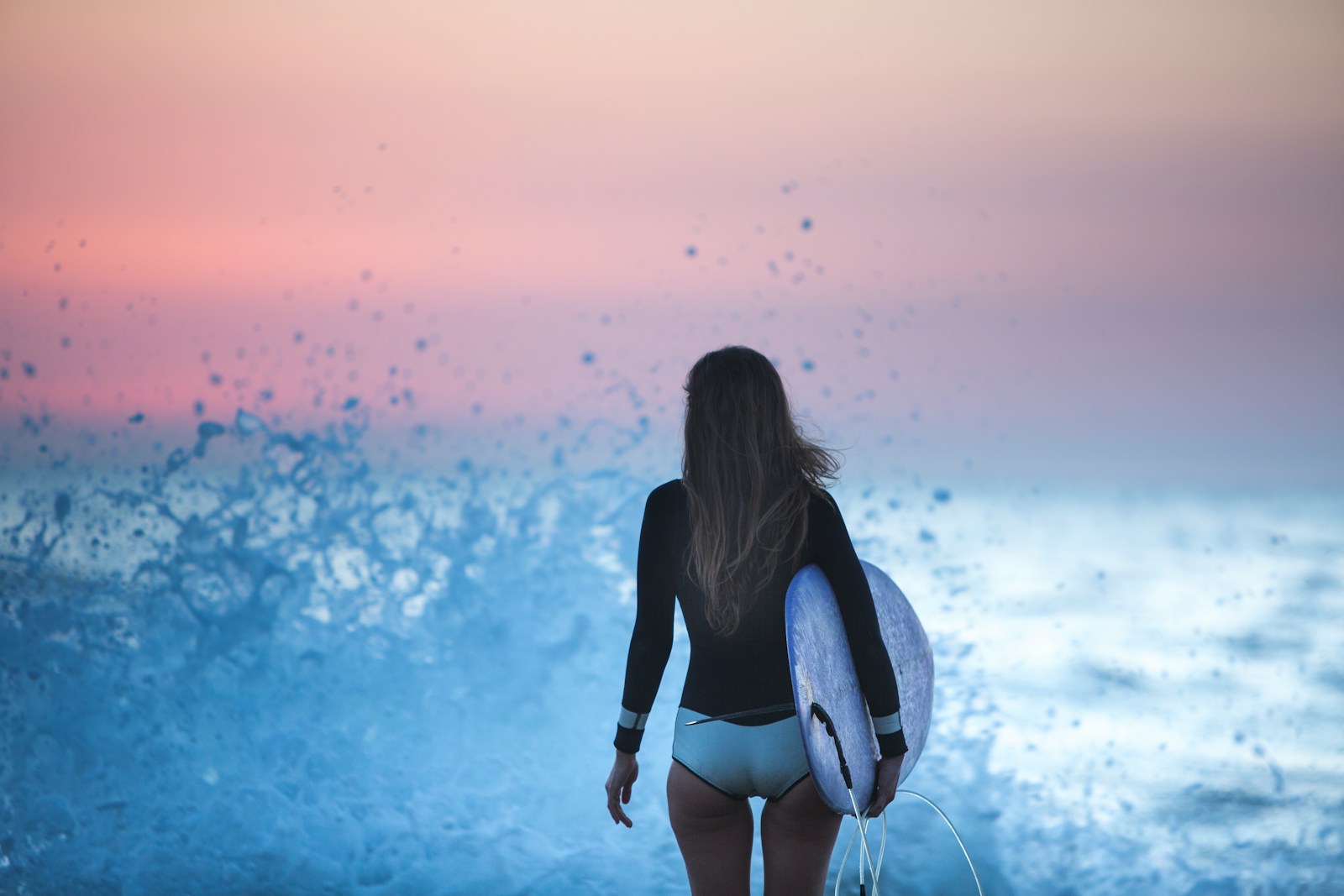 黒の長袖ラッシュガードで夕暮れの海に立つ女性