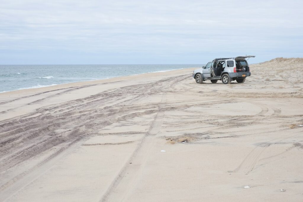 冬の砂浜に止まるサーフボードを積んだ車とタイヤの轍