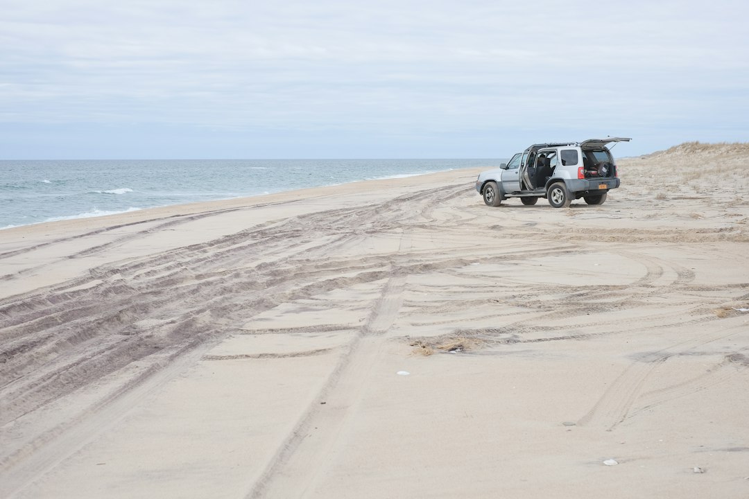 冬の砂浜に止まるサーフボードを積んだ車とタイヤの轍