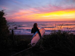 ウェットスーツを着た女性サーファーが夕暮れの海辺でサーフボードを抱えている